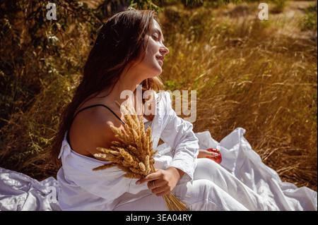 Profil einer Frau, die auf goldenem Feld mit getrocknetem Gras sitzt Stockfoto