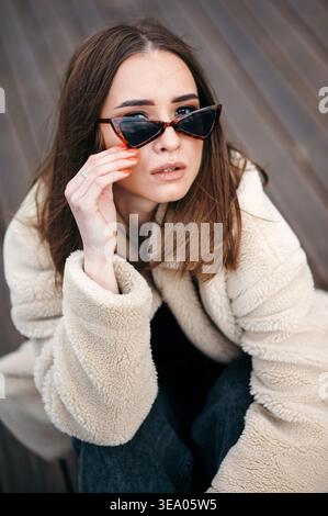 Modische Frau in Sonnenbrille, die auf dem Dach sitzt Stockfoto