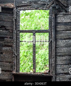 Verkohlter Holzfensterrahmen eines abgebrannten Hauses. Verbrannte Holzwand nach Feuer Stockfoto