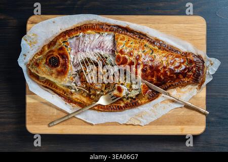 Traditioneller Karpfencoulibiac Fischkuchen in Fischform, Nahaufnahme. Gebackener Fisch Coulibiac Kuchen in Form eines Fisches gefüllt mit Karpfen und Pilzen auf einem hölzernen bo Stockfoto