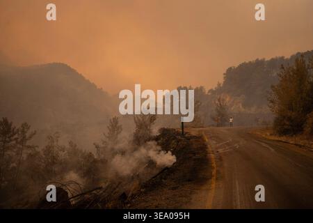 Rauch weht aus einem brennenden Bereich in der Nähe einer Straße, mit Hügeln im Hintergrund. Stockfoto