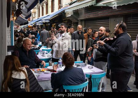 Eine Gruppe von Musikern spielt Instrumente an Tischen im Freien in einer belebten Straße voller Menschen. Stockfoto