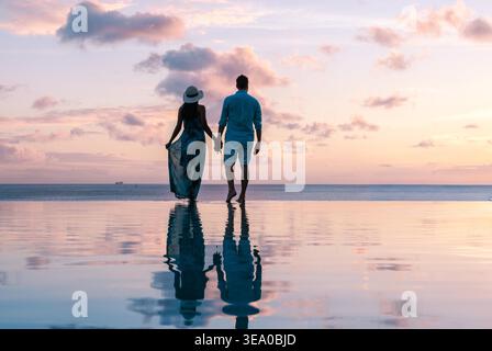 Ein Paar genießt einen romantischen Spaziergang entlang der glitzernden Küste von Saint Lucia bei Sonnenuntergang. Die leuchtenden Farben des Himmels spiegeln sich wunderbar auf dem ruhigen Wasser wider und schaffen eine ruhige Atmosphäre. Stockfoto