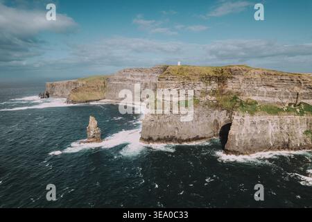 Aus der Vogelperspektive treffen auf den turbulenten Atlantik, Wellen krachen gegen den Stein und ein scharf weißer Leuchtturm beobachtet von oben Doolin, IRE Stockfoto