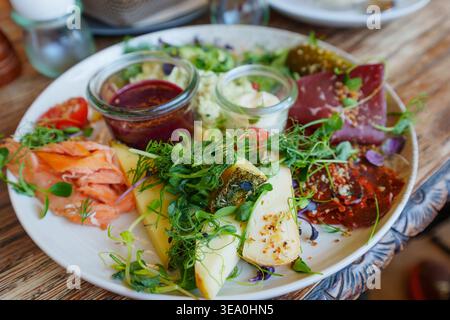 Gourmet-Vorspeiseteller mit Räucherlachs, handwerklichem Käse, Wurstwaren und frischem Mikrogrün, serviert auf einem rustikalen Holztisch in einem deutschen Café Stockfoto