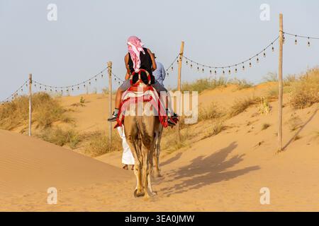 Rückansicht von Touristen, die auf einem Kamel auf einer Wüstensafari durch die Dünen in Dubai, VAE, reiten. Stockfoto