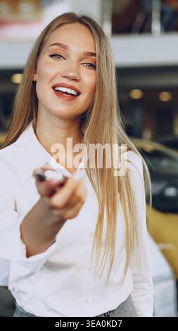 Frau lächelt tagsüber, während sie Autoschlüssel in einem Händlerbetrieb hält Stockfoto