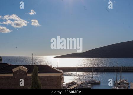 Heller Küstenhafen mit Booten, ruhigem Meer und sonnigem Horizont unter klarem blauem Himmel. Stockfoto