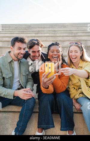 Eine Gruppe fröhlicher Freunde, die gerne einen Moment beim Betrachten ihres Smartphones verbringen und ihre Freude und ihr Lachen in einer reizvollen Interaktion zum Ausdruck bringen Stockfoto