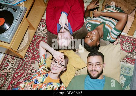 Multiethnische Erwachsene Freunde, die sich während des Vinyl-Hörens auf dem Boden entspannen Stockfoto