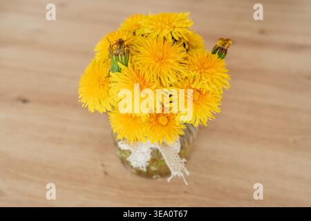 Gelber Löwenzahn in Glas auf Holztisch. Natürliche Einrichtung und Frühlingsstimmung. Zusammensetzung und Kopierraum reinigen. Stockfoto