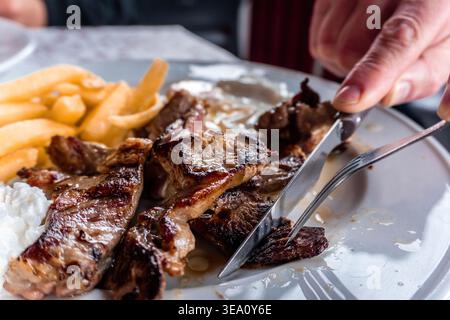 Person, die gegrilltes Steak und Pommes frites schneidet Stockfoto