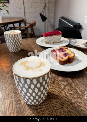 Cappuccino mit herzförmigem Schaum und Beerenkuchen auf einem Holztisch in einem gemütlichen Café. Mobiles Foto Stockfoto