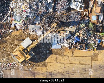 Luftaufnahme einer Ressourcenrückgewinnungsanlage mit einem Bagger, der Schrott und Schutt zwischen den Anhäufungen von Industrieabfällen in Taiwan transportiert. Stockfoto
