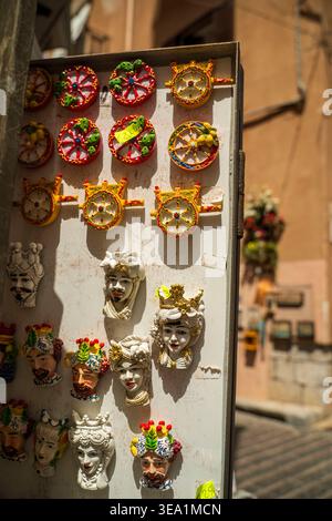 Farbenfrohe sizilianische Keramikdekorationen auf weiß getünchten Wänden in Sizilien, Italien. Traditionelle handgefertigte Keramikmasken und dekorative Räder mit Stockfoto