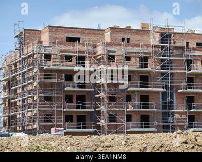 Mehrstöckiges Wohngebäude im Bau mit roten Ziegelwänden und umfangreichem Stahlgerüstsystem unter blauem Himmel. Mijas Costa, Málaga. Stockfoto