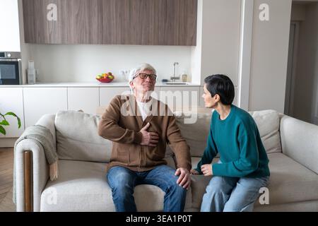 Besorgte ältere Ehefrau mit besorgtem, verängstigten Ausdruck, der auf einen Mann mit Herzinfarkt blickt. Stockfoto