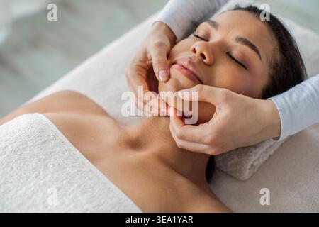 Junge afroamerikanische Frau bekommt Gesichtsmassage im Spa-Salon Stockfoto