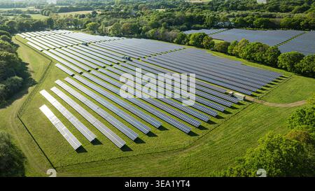Ein Blick aus der Vogelperspektive zeigt einen weitläufigen Solarpark mit Reihen von Solarpaneelen inmitten einer grünen Landschaft unter sonnigem Himmel. Stockfoto