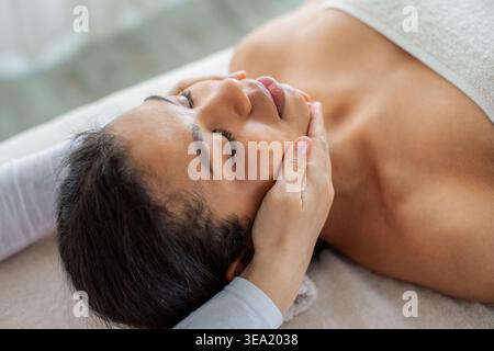 Junge schöne afroamerikanische Frau, die eine sanfte Kinnmassage im Spa bekommt Stockfoto