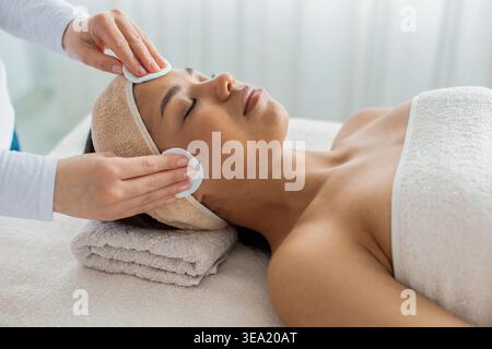 Spa-Therapeutin, die eine Gesichtsreinigung mit Wattepads für schwarze Frau durchführt Stockfoto