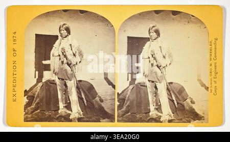 Shee-zah-nan-tan, Jicarilla Apache Brave in charakteristischer Tracht, Nord-New Mexico, Nr. 42 aus der Serie Geographical Explorations and Surveys West of the 100th Meridian von Timothy O’Sullivan, 1874, Stereogramm eines jungen Apachen in traditioneller Kleidung, der mit Gewehr und Decke steht Stockfoto