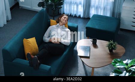 Blick von oben auf die Geschäftsfrau, die am Laptop arbeitet, während sie auf dem Sofa liegt. Kaukasischer Projektmanager, der Computer verwendet, um zu kommunizieren, während er Umsätze meldet Stockfoto