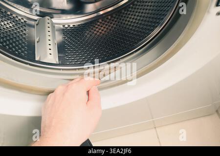 Verschmutztes, schimmeliges Dichtgummi der Waschmaschine. Die Person prüft den Schmutz auf dem Gummi einer Waschmaschine. Abgeschnittene Handwaschmaschine. Gummi Stockfoto