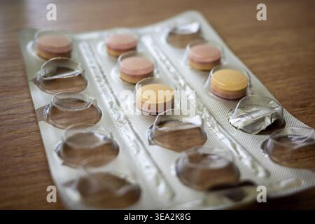 Eine Blisterpackung enthält gelbe, rosafarbene und orangene Tabletten. Die Packung wird auf einen Holztisch gestellt. Licht leuchtet auf die Oberfläche und hebt die Formen des hervor Stockfoto