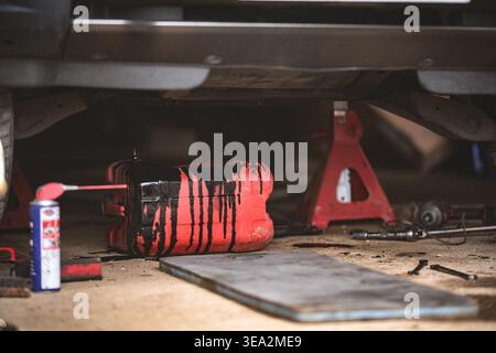 Eine Nahaufnahme eines Autos, an dem mit Werkzeugen und Ausrüstung gearbeitet wird. Der rote Ölbehälter ist mit Öl verschmutzt. Stockfoto