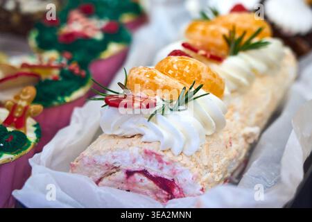 Meringue-Roulette mit Schlagsahne, Mandarinenscheiben und Rosmarin. Pavlova-Rolle mit Beerenfüllung auf einem festlichen Desserttisch. Stockfoto
