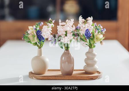 Tisch mit Frühlingsblumen in Vasen auf Holztablett zu Hause dekoriert. Nahaufnahme von drei kleinen Blumenstraußen, die von einem Schrank aufgestellt wurden Stockfoto
