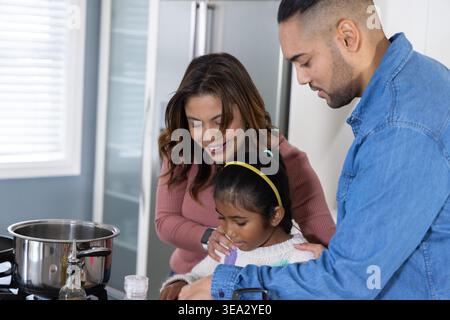 Eltern und Tochter bereiten Essen an der Küchentheke mit Edelstahltopf, Ölflasche, Shaker vor Stockfoto