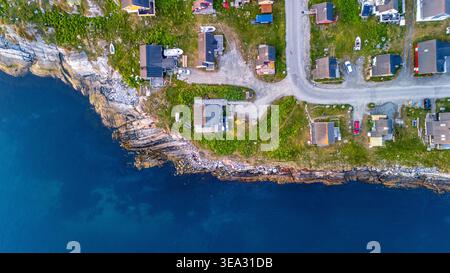 Blick aus der Vogelperspektive auf farbenfrohe Häuser an einer felsigen Küste mit tiefblauem Wasser und üppigem grünem Gras in Nuuk, Sermersooq, Grönland. Stockfoto