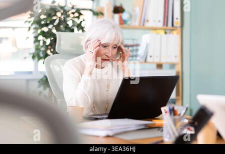 Müde, ältere Frau arbeitet am Laptop Stockfoto