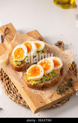 Zwei Scheiben knuspriger Sauerteig mit cremigem Avocadopüree und marmelierten mittelgekochten Eiern. Weiches natürliches Morgenlicht hebt die Texturen von t hervor Stockfoto