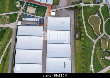 Blick aus der Vogelperspektive auf moderne Industriegebäude mit grauen Dächern, umgeben von grünen Rasenflächen, Wanderwegen und einem kleinen Teich in Reggello, Toskana, Italien. Stockfoto