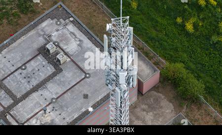 Luftaufnahme eines Telekommunikationsturms mit mehreren Antennen und Schüsseln neben einem Dach des Gebäudes in Almere, Flevoland, Niederlande. Stockfoto