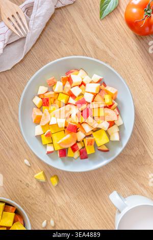 Eine Nahaufnahme mit frischem Obst- und Gemüsesalat in einer Schüssel mit Tomaten, Apfel und einer Tasse Milch auf einem Holzteller. Draufsicht. Flache Lagen. Stockfoto