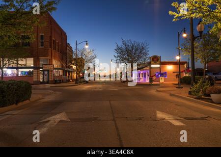 Winslow, USA, Kreuzung mit der Route 66, die in der Abenddämmerung mit historischen Gebäuden und Geschäften auf der Straße gemalt ist. Farbenfroher Himmel Stockfoto