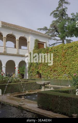 Springbrunnen-Pool mit Steinbecken und Jets neben einer zweistöckigen Arkadengalerie, die in Herbstelfeu in den historischen Alhambra-Gärten in Granada, Andalusien, liegt Stockfoto
