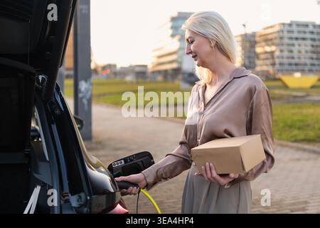 Aktivieren des Ladevorgangs für Elektrofahrzeuge, während eine Lieferbox an einer städtischen Station gehalten wird. Stockfoto