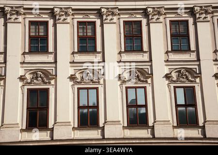 Verzierte historische Gebäudefassade mit Fensterreihen und dekorativen Skulpturenelementen in Wien, die klassische architektonische Details zeigen Stockfoto