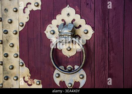 Kunstvoller Metallklopfer, montiert an einer Holztür mit dekorativen Platten und Nieten, fotografiert in Wien, Österreich. Stockfoto