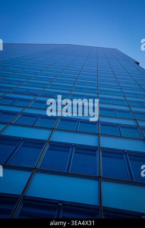 Die Glasfassade des Bürogebäudes erhebt sich gegen den klaren blauen Himmel, moderne Hochhausarchitektur mit reflektierenden Fenstern und geometrischem Gittermuster. Stockfoto