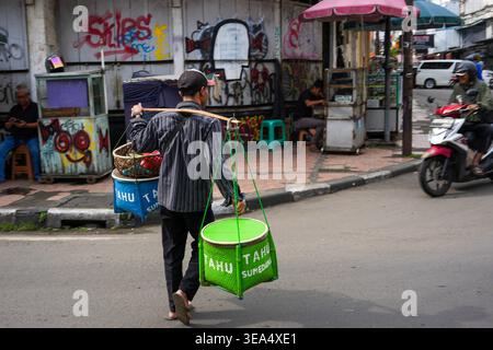 Bandung, Indonesien - 2. Februar 2026 - Ein traditioneller indonesischer Straßenkostverkäufer balanciert einen Bambusstock mit Körben Tahu Sumedang Tofu während wa Stockfoto