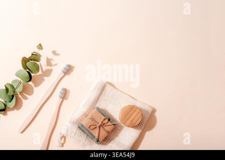 Umweltfreundliche Badezimmer-Accessoires mit Bambus-Zahnbürsten, natürlicher Seife und Eukalyptuszweig auf beigem Hintergrund im Sonnenlicht. Draufsicht, flach, Co Stockfoto