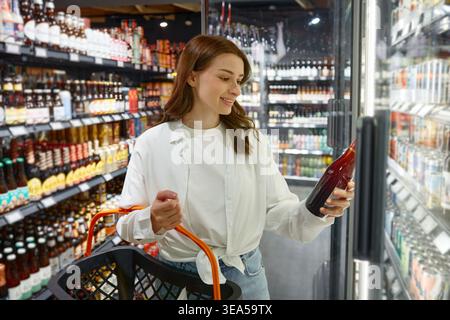 Eine Frau schaut sich eine Flasche Bier in einem Supermarkt an Stockfoto