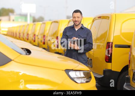 Mechaniker mit Klemmbrett, der auf einem Parkplatz vor gelben Lieferwagen steht Stockfoto