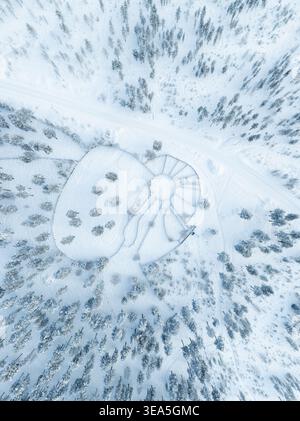 Blick aus der Vogelperspektive auf eine traditionelle Rentierkorral, umgeben von einem dichten, tief verschneiten Kiefernwald in Lappland, Finnland. Stockfoto